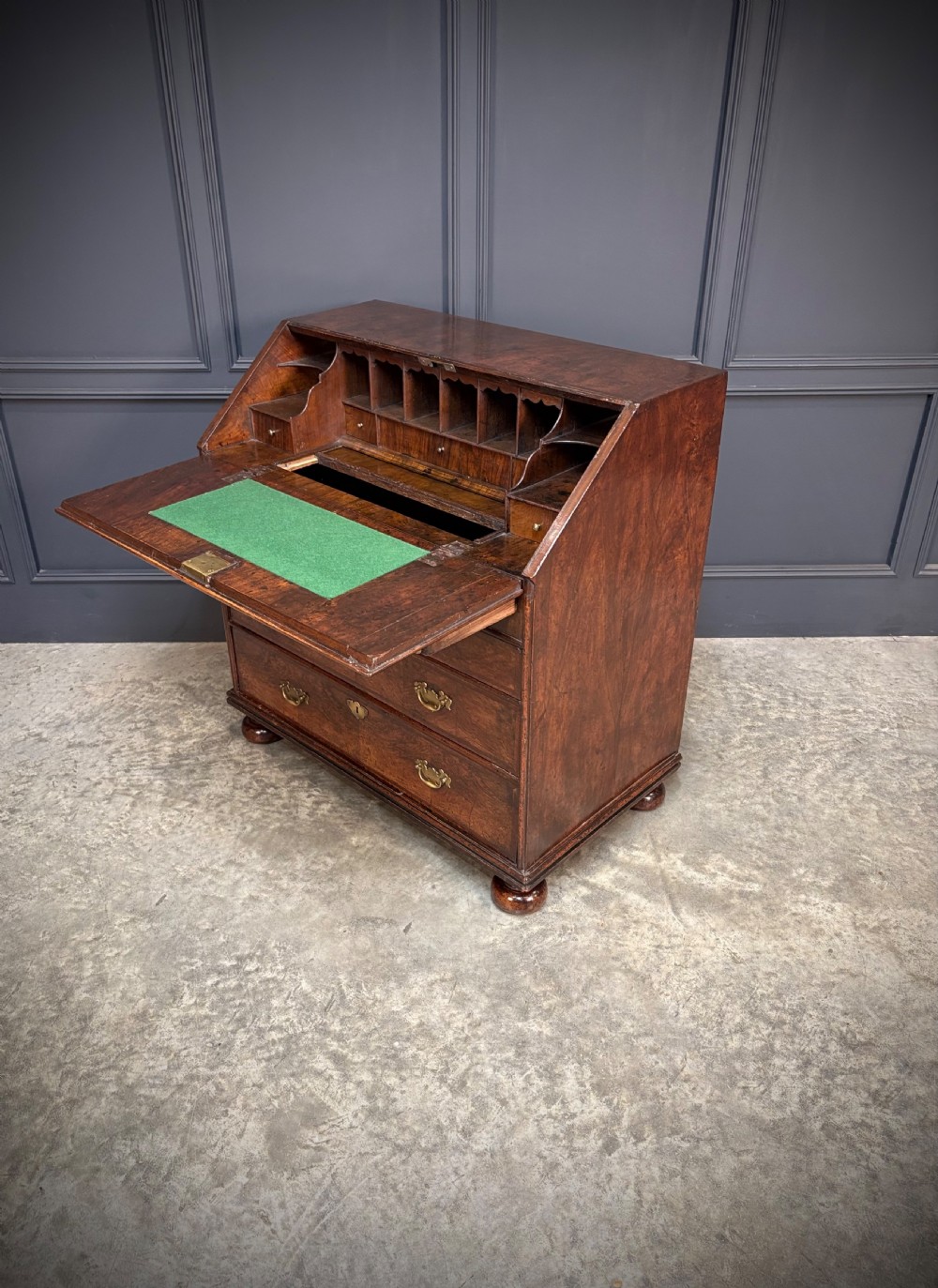 An antique Queen Anne walnut bureau featuring a sloping write-down front above drawers with brass handles, raised on compressed bun feet. View VIII