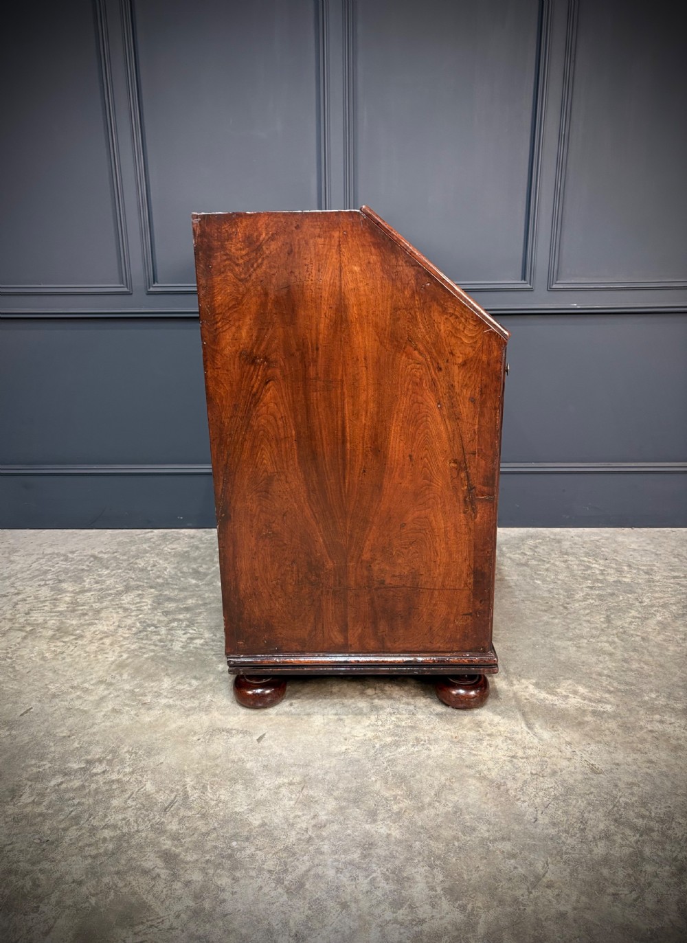 An antique Queen Anne walnut bureau featuring a sloping write-down front above drawers with brass handles, raised on compressed bun feet. View XII