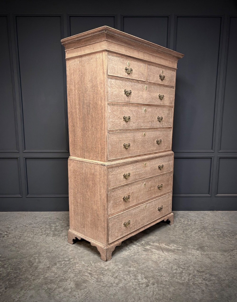 An 18th-century bleached oak chest on chest with stacked upper and lower drawer sections, brass drop handles, and bracket feet.