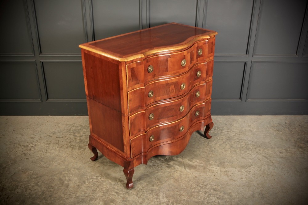 An antique walnut serpentine-front chest featuring four drawers with brass ring pull handles resting on carved cabriole feet.