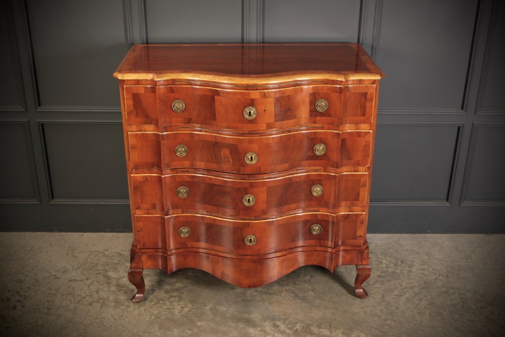 An antique walnut serpentine-front chest featuring four drawers with brass ring pull handles resting on carved cabriole feet. View V