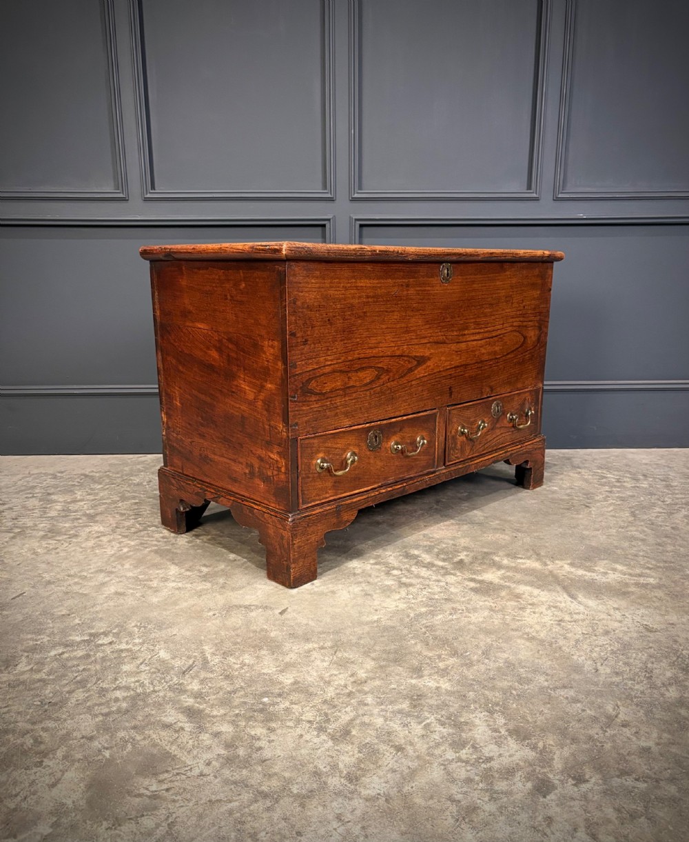 A Georgian elm blanket box featuring a hinged top lid, two lower drawers with brass swan-neck handles, and shaped bracket feet. View IV