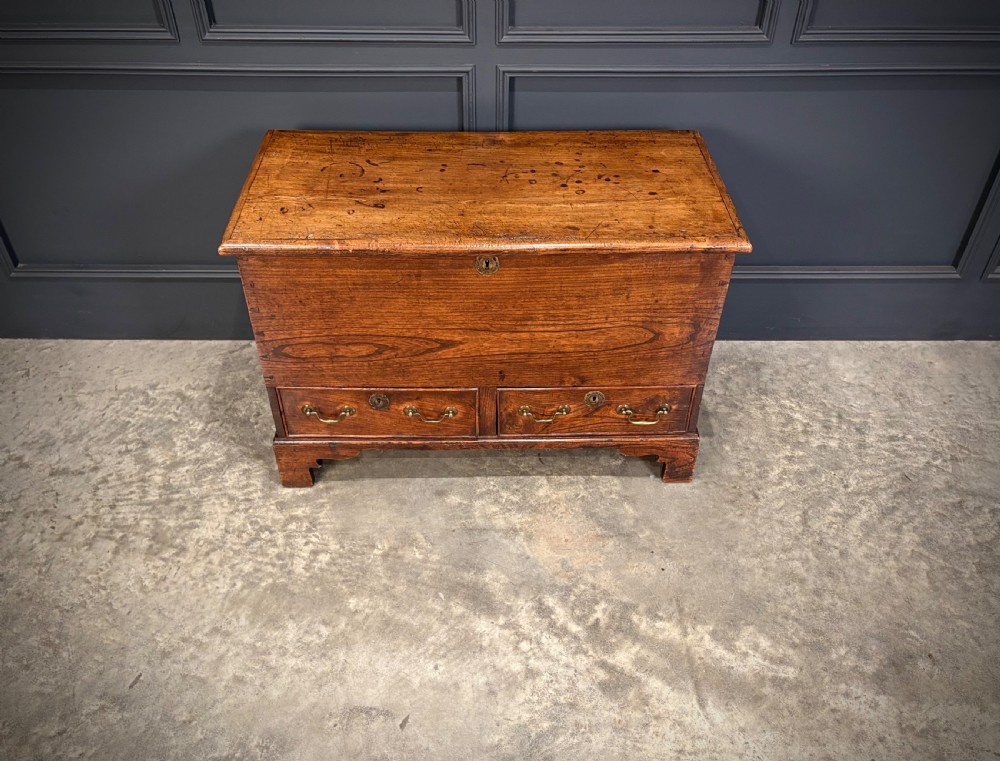 A Georgian elm blanket box featuring a hinged top lid, two lower drawers with brass swan-neck handles, and shaped bracket feet. View VII