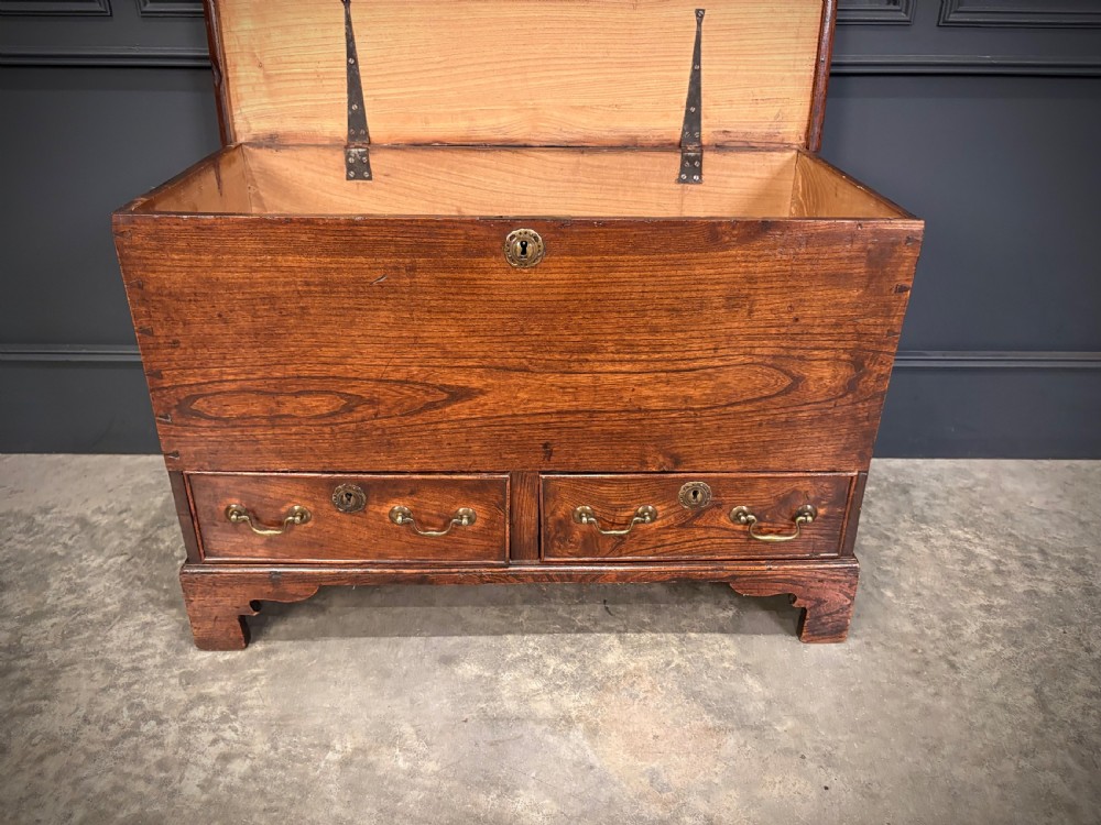 A Georgian elm blanket box featuring a hinged top lid, two lower drawers with brass swan-neck handles, and shaped bracket feet. View XI