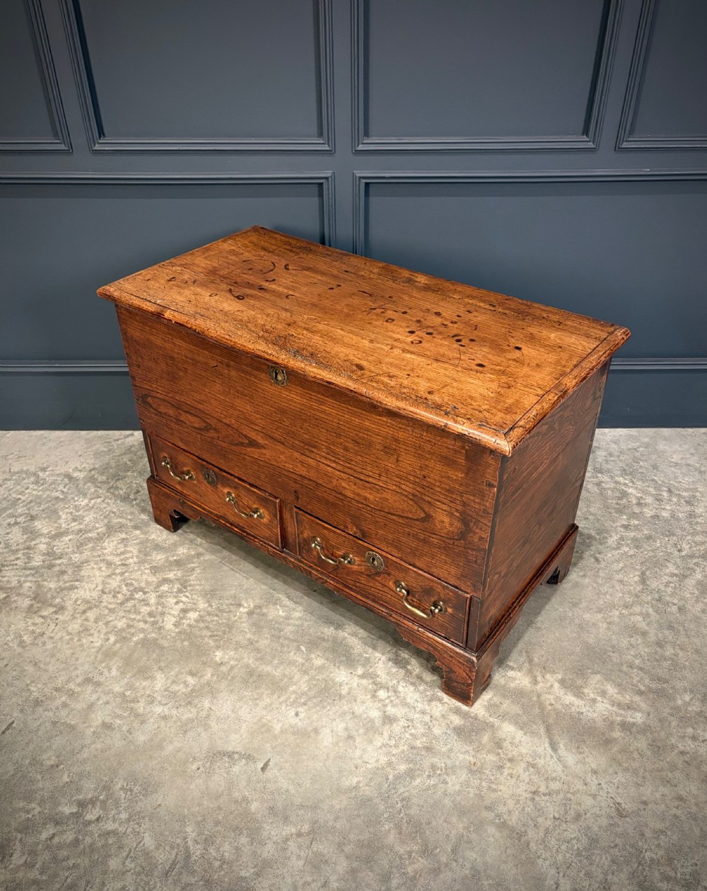 A Georgian elm blanket box featuring a hinged top lid, two lower drawers with brass swan-neck handles, and shaped bracket feet. View XII
