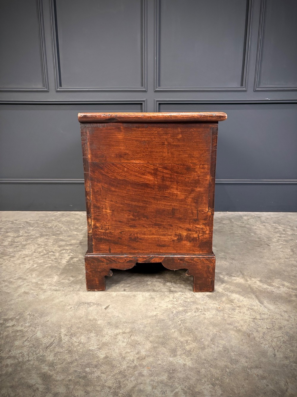 A Georgian elm blanket box featuring a hinged top lid, two lower drawers with brass swan-neck handles, and shaped bracket feet. View XVI