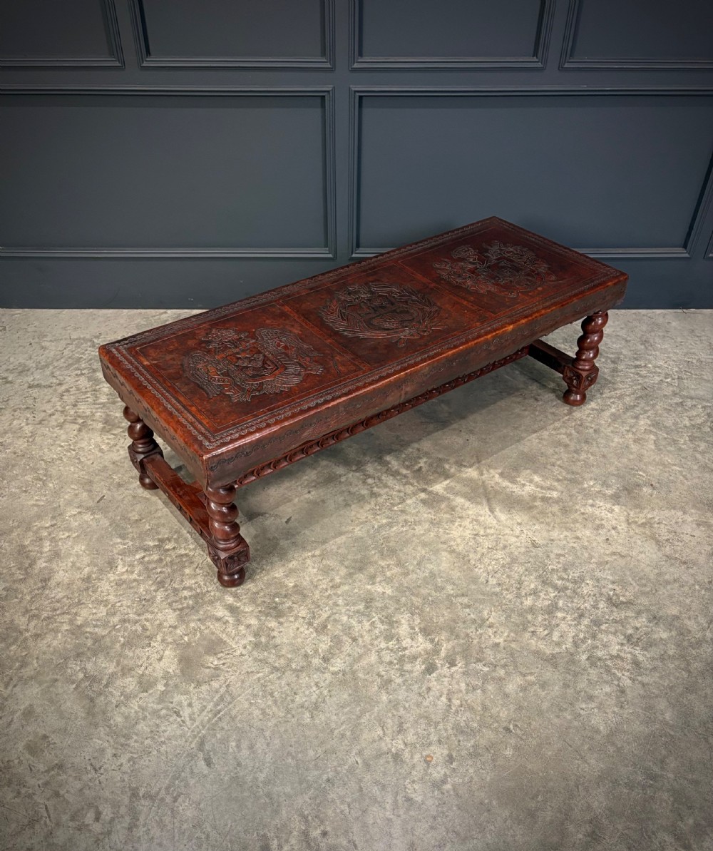 A low rectangular mahogany coffee table featuring three embossed leather top panels depicting heraldic coats of arms and supported by turned legs. View IV