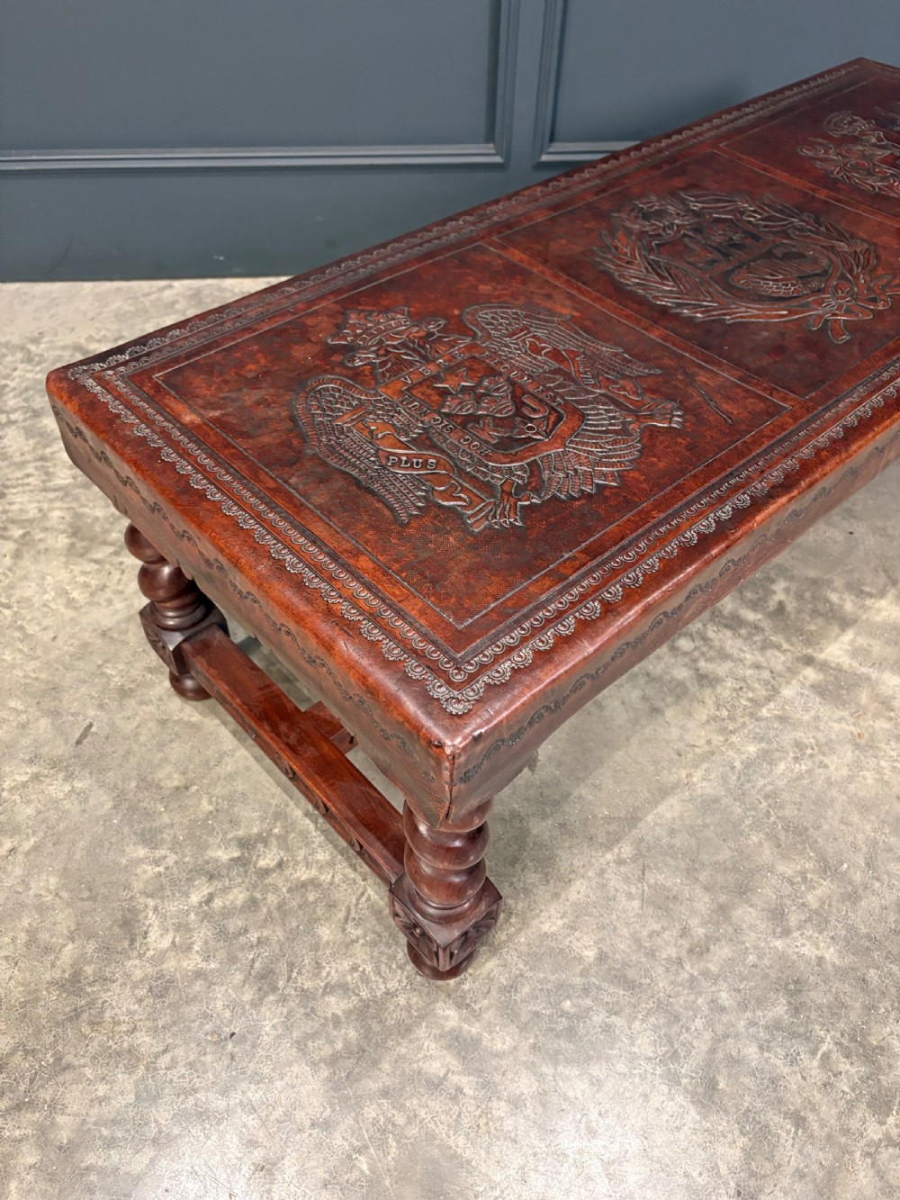 A low rectangular mahogany coffee table featuring three embossed leather top panels depicting heraldic coats of arms and supported by turned legs. View II
