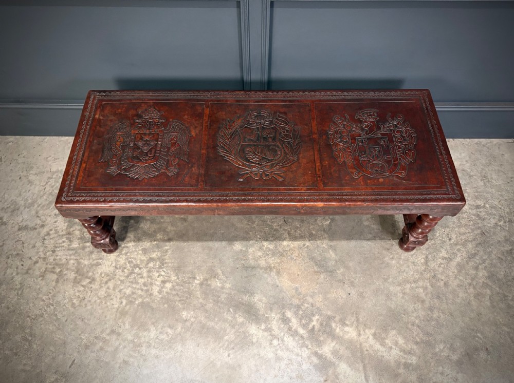 A low rectangular mahogany coffee table featuring three embossed leather top panels depicting heraldic coats of arms and supported by turned legs. View III