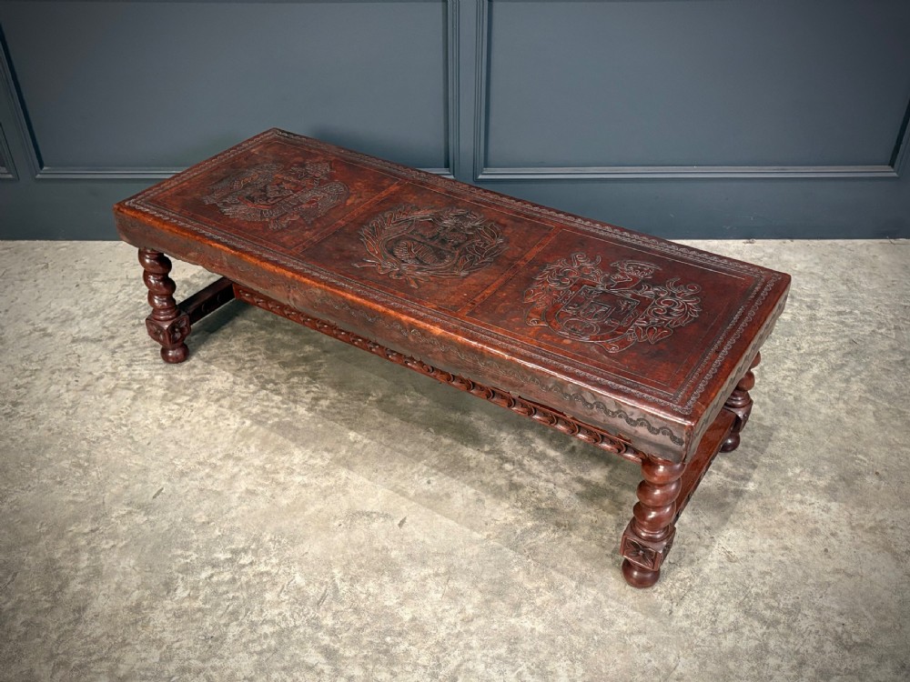 A low rectangular mahogany coffee table featuring three embossed leather top panels depicting heraldic coats of arms and supported by turned legs.
