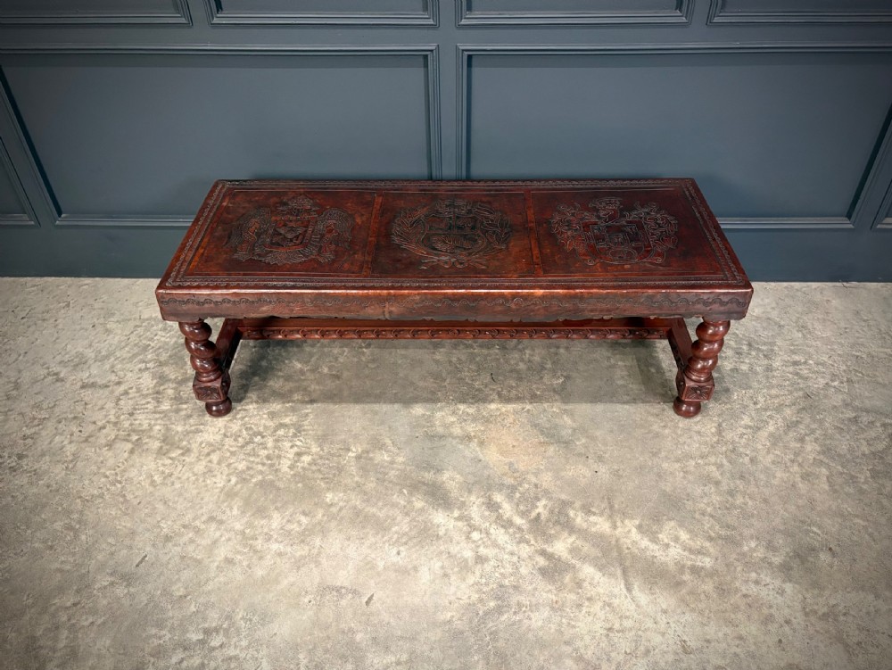 A low rectangular mahogany coffee table featuring three embossed leather top panels depicting heraldic coats of arms and supported by turned legs. View V