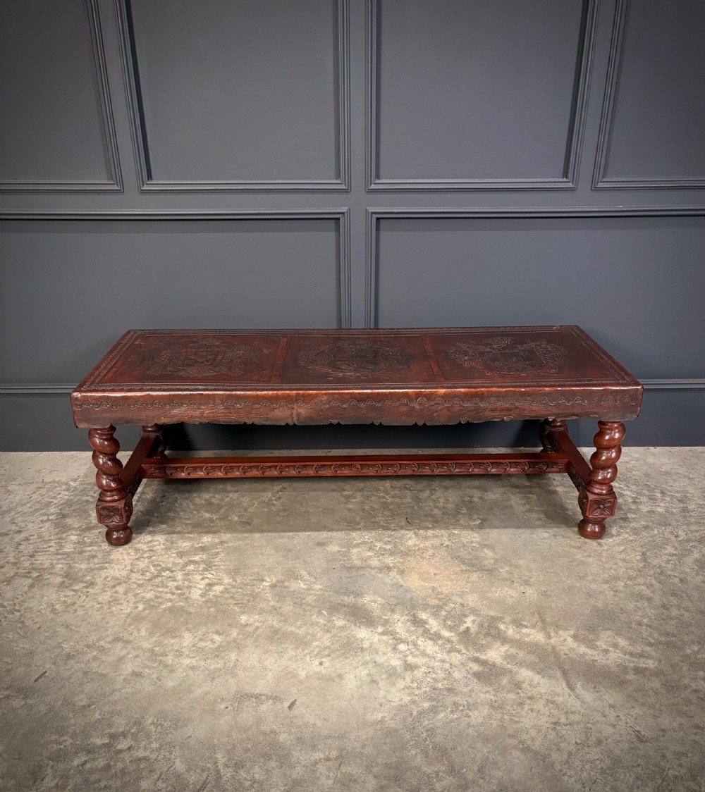 A low rectangular mahogany coffee table featuring three embossed leather top panels depicting heraldic coats of arms and supported by turned legs. View IX