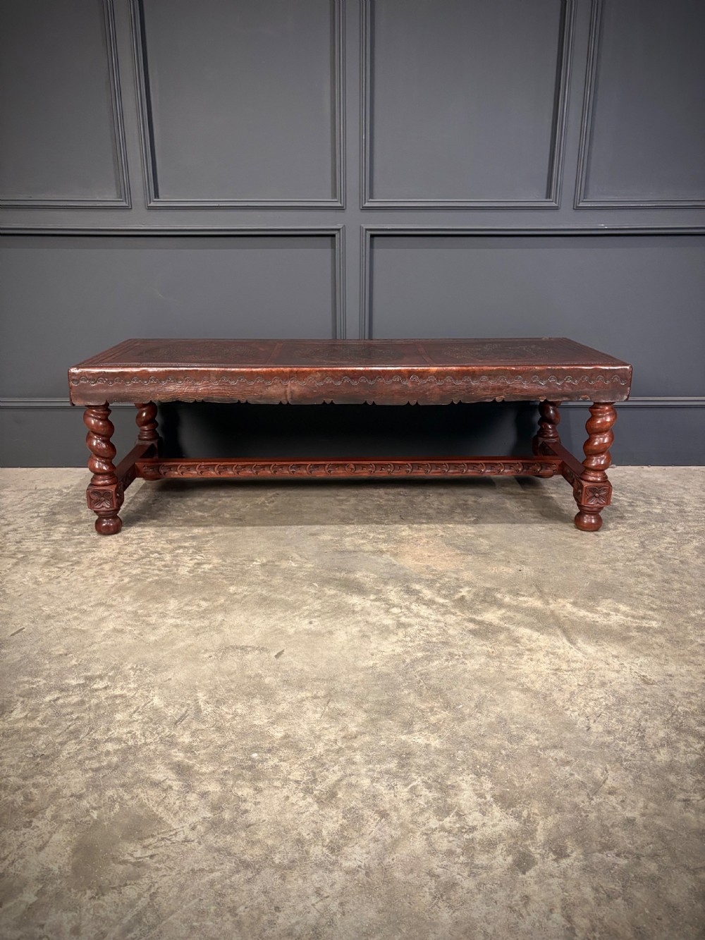 A low rectangular mahogany coffee table featuring three embossed leather top panels depicting heraldic coats of arms and supported by turned legs. View X