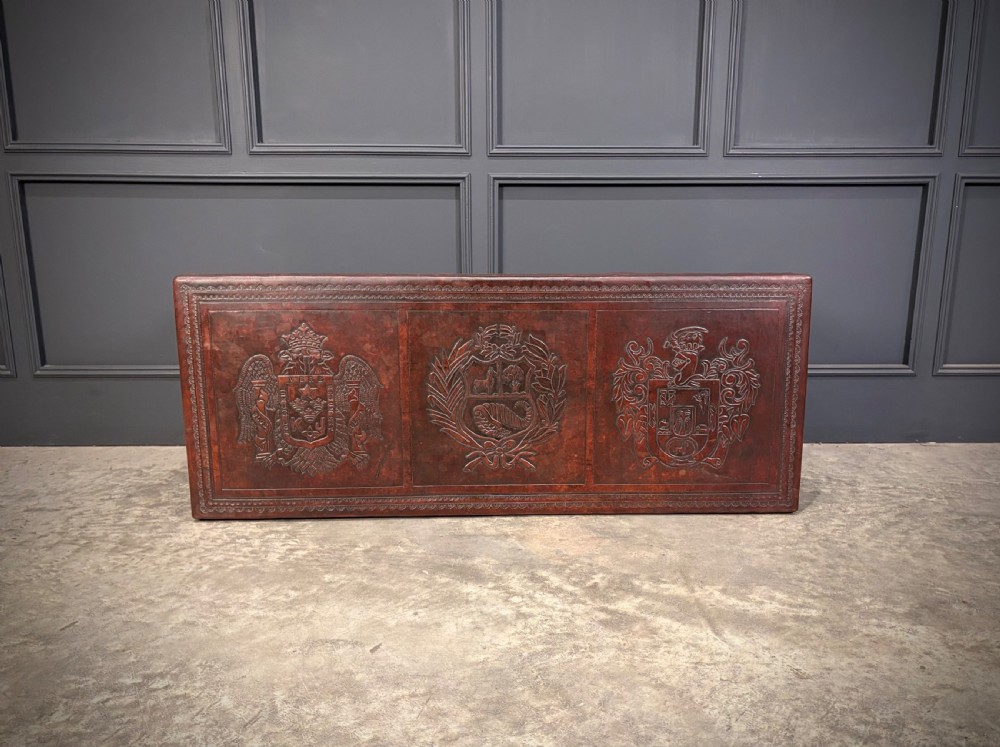 A low rectangular mahogany coffee table featuring three embossed leather top panels depicting heraldic coats of arms and supported by turned legs. View XII