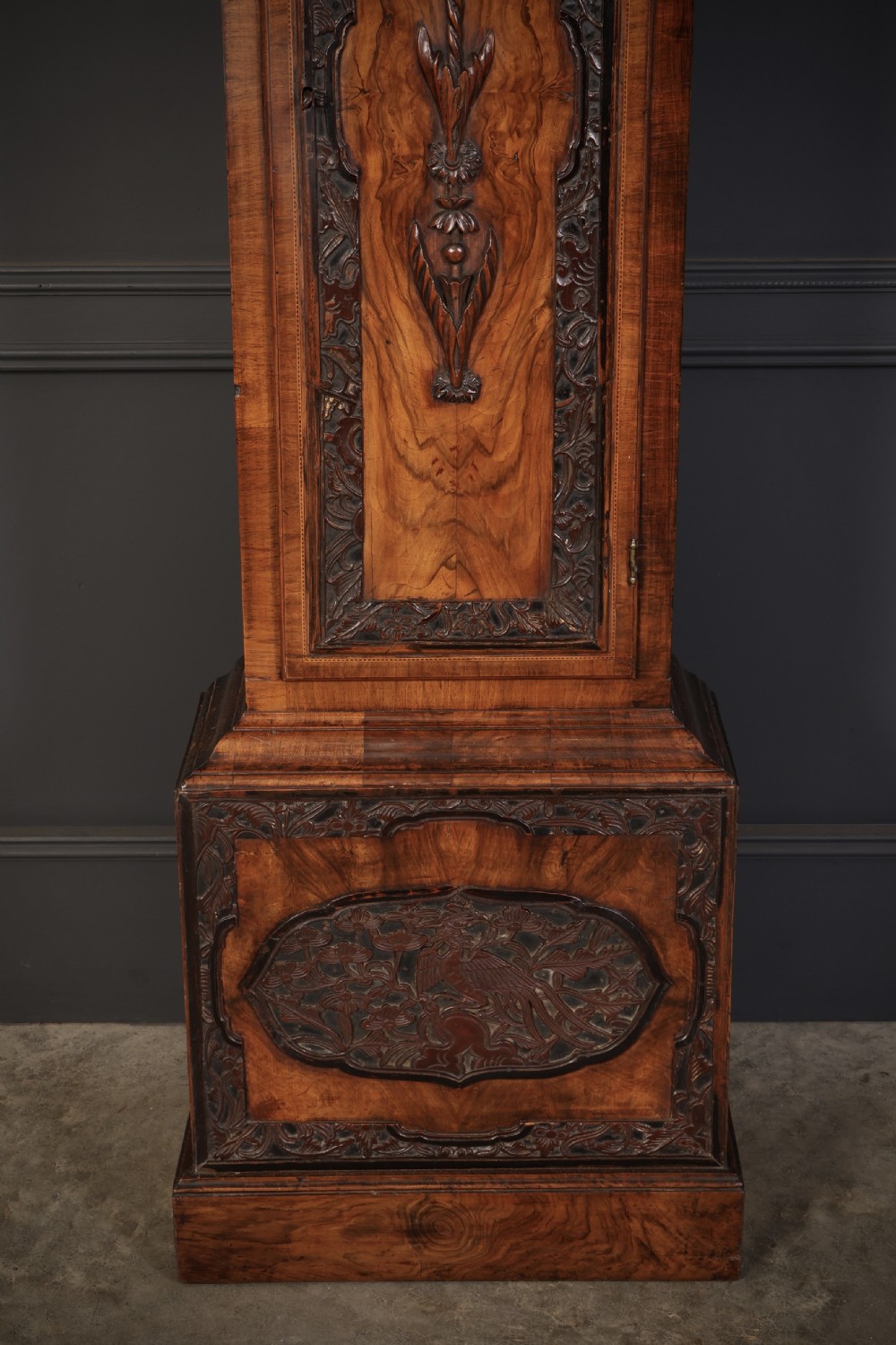 An 18th-century carved walnut longcase clock featuring an arched hood, brass dial with silvered chapter ring, and decorative carved central door panel. View III