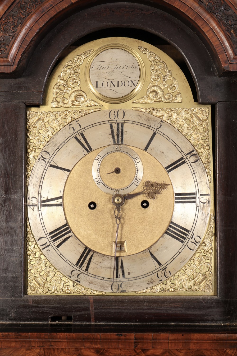 An 18th-century carved walnut longcase clock featuring an arched hood, brass dial with silvered chapter ring, and decorative carved central door panel. View XI