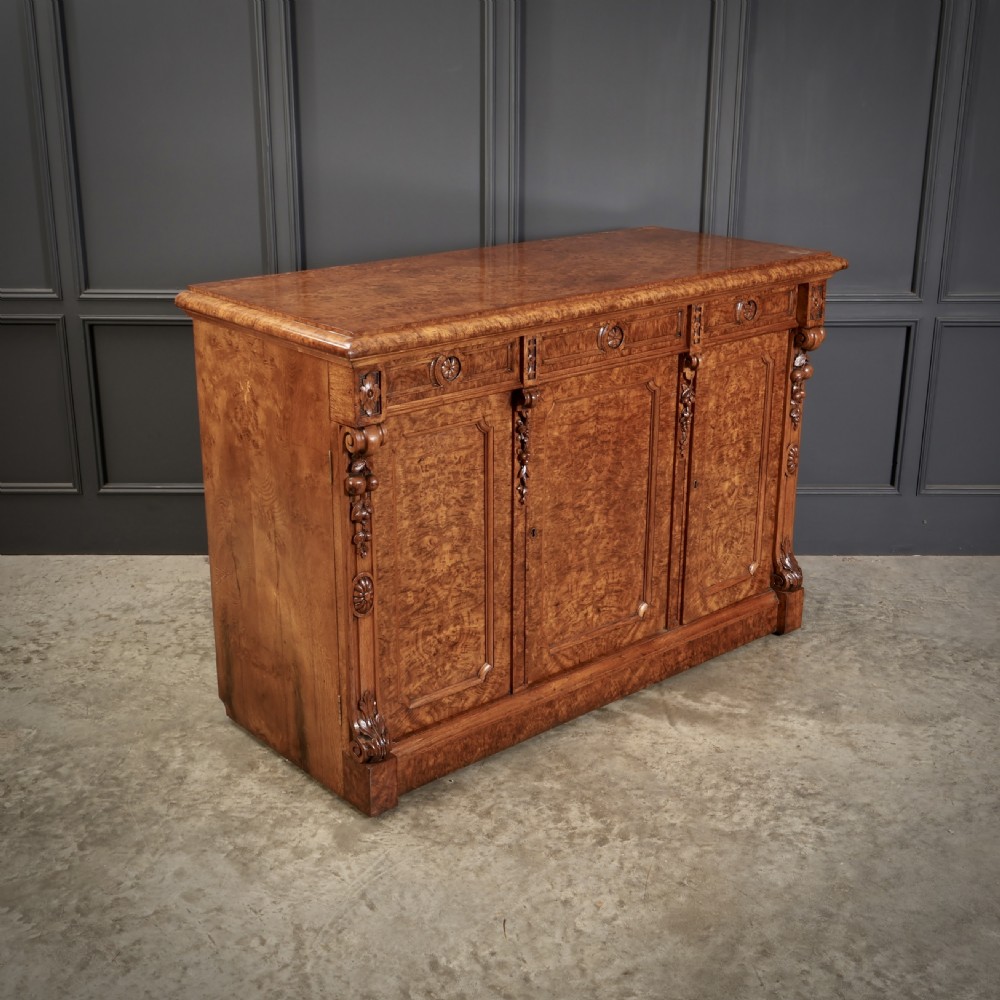 A Victorian pollard oak sideboard featuring three panelled cupboard doors, carved foliage pilasters, and a moulded rectangular top.
