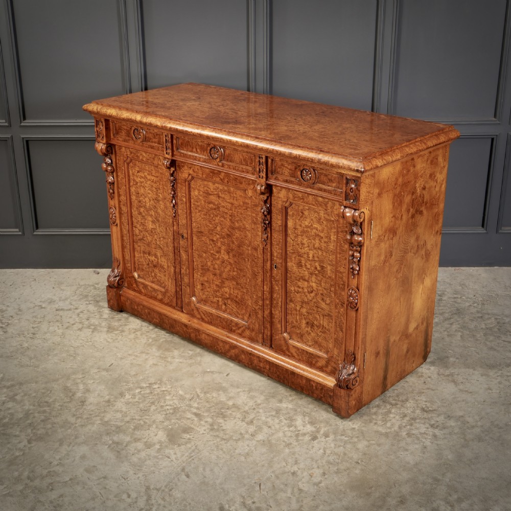 A Victorian pollard oak sideboard featuring three panelled cupboard doors, carved foliage pilasters, and a moulded rectangular top. View XI