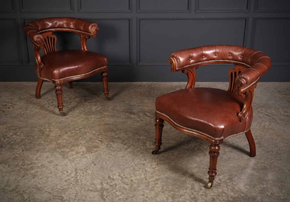 A pair of Victorian mahogany captains desk chairs featuring button-tufted brown leather horseshoe armrests, padded leather seats with studding, turned front legs, and brass castors.