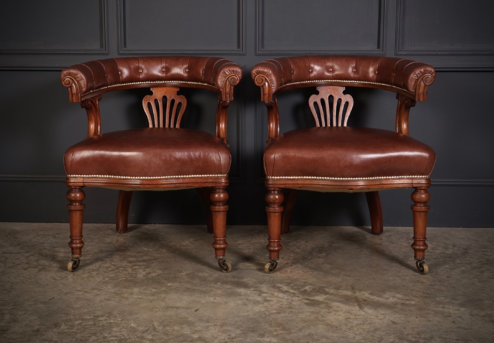 A pair of Victorian mahogany captains desk chairs featuring button-tufted brown leather horseshoe armrests, padded leather seats with studding, turned front legs, and brass castors. View II