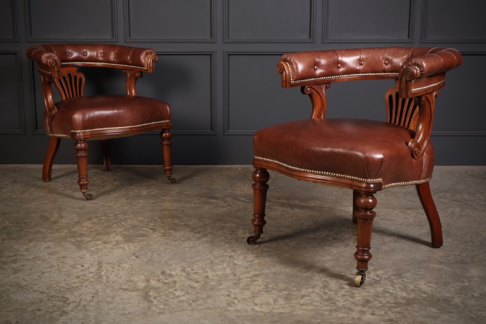 A pair of Victorian mahogany captains desk chairs featuring button-tufted brown leather horseshoe armrests, padded leather seats with studding, turned front legs, and brass castors. View III