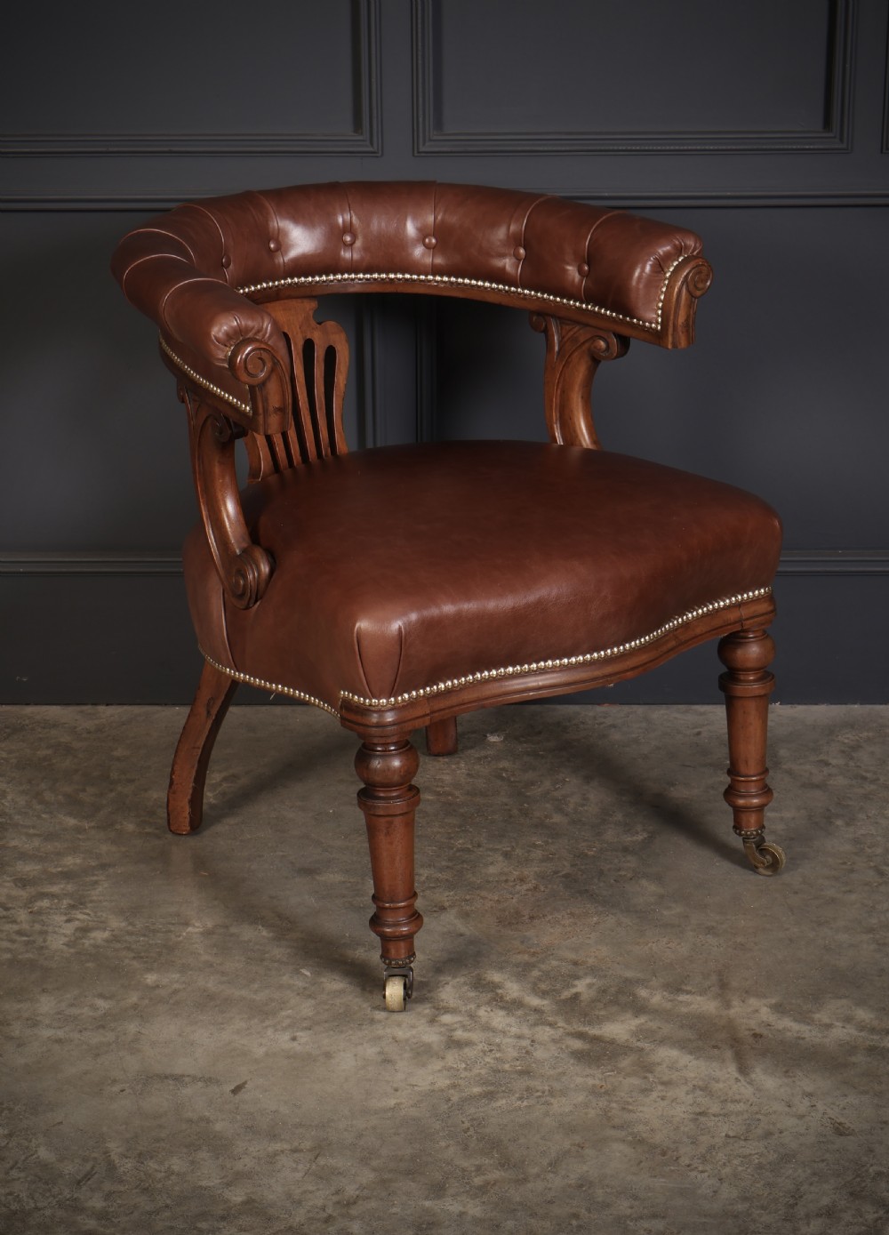 A pair of Victorian mahogany captains desk chairs featuring button-tufted brown leather horseshoe armrests, padded leather seats with studding, turned front legs, and brass castors. View IV