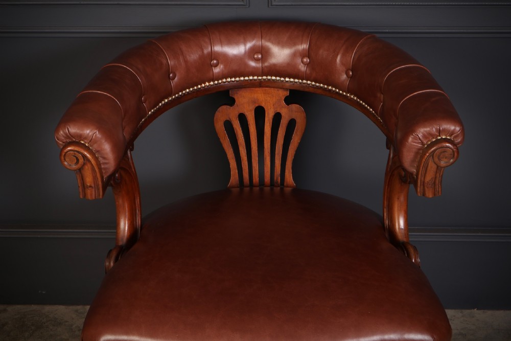 A pair of Victorian mahogany captains desk chairs featuring button-tufted brown leather horseshoe armrests, padded leather seats with studding, turned front legs, and brass castors. View VII
