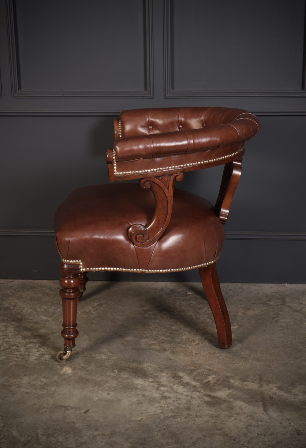 A pair of Victorian mahogany captains desk chairs featuring button-tufted brown leather horseshoe armrests, padded leather seats with studding, turned front legs, and brass castors. View IX