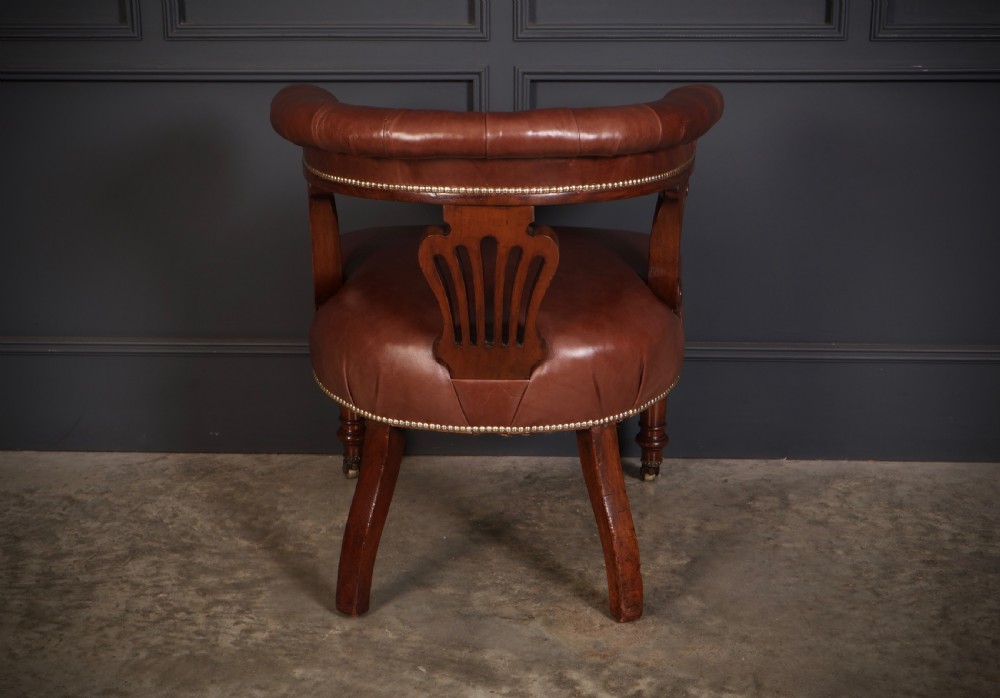 A pair of Victorian mahogany captains desk chairs featuring button-tufted brown leather horseshoe armrests, padded leather seats with studding, turned front legs, and brass castors. View X