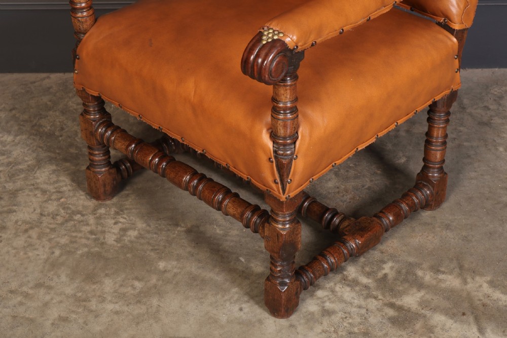 A nineteenth-century wingback armchair featuring tan leather upholstery with brass stud detailing, carved oak scroll armrests, and turned legs with connecting stretchers. View IV