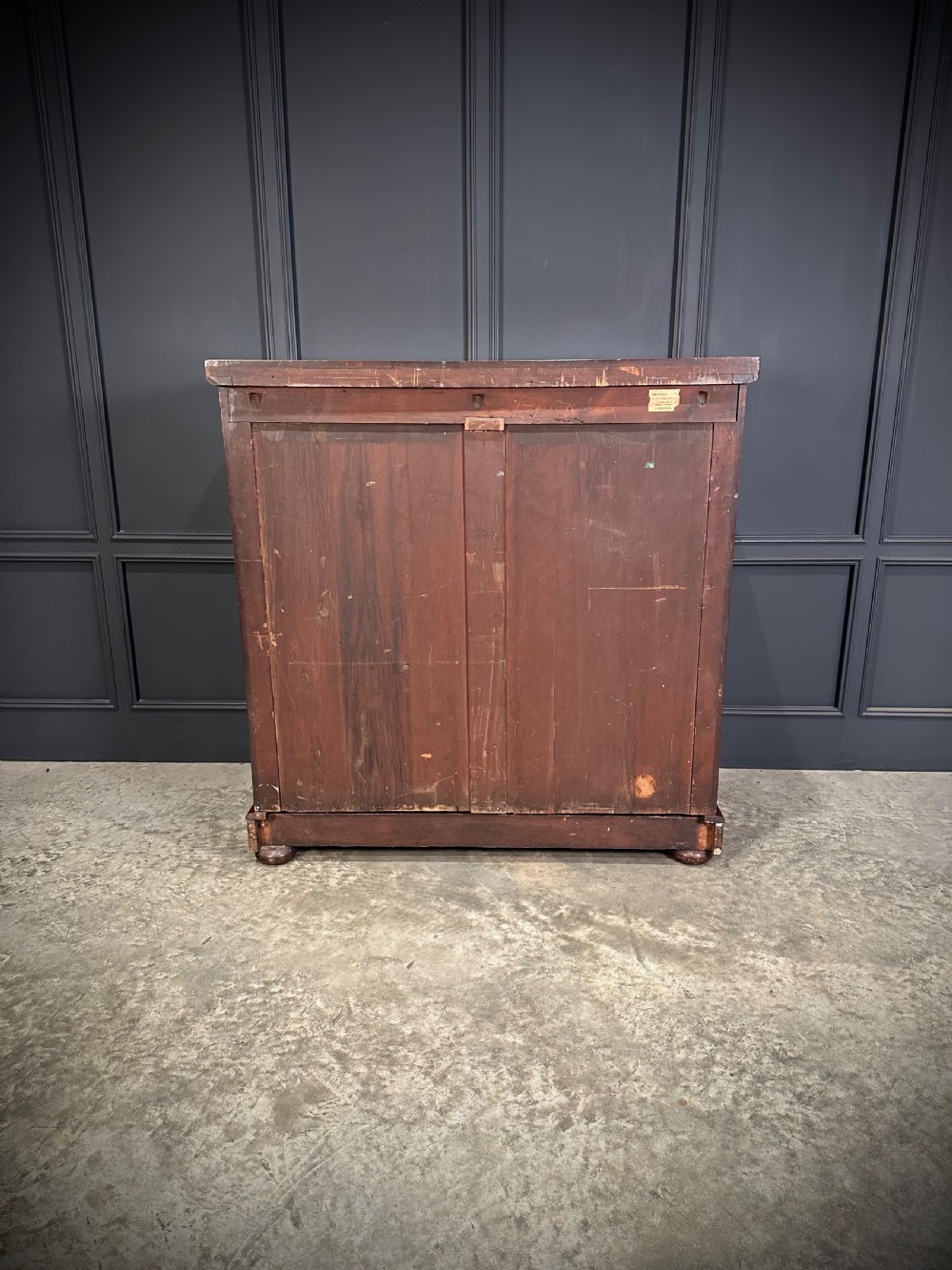 A tall Victorian flame mahogany chest of drawers featuring a decorative top drawer, five lower drawers with dark turned handles, rounded pilasters, and a solid plinth base. View XI