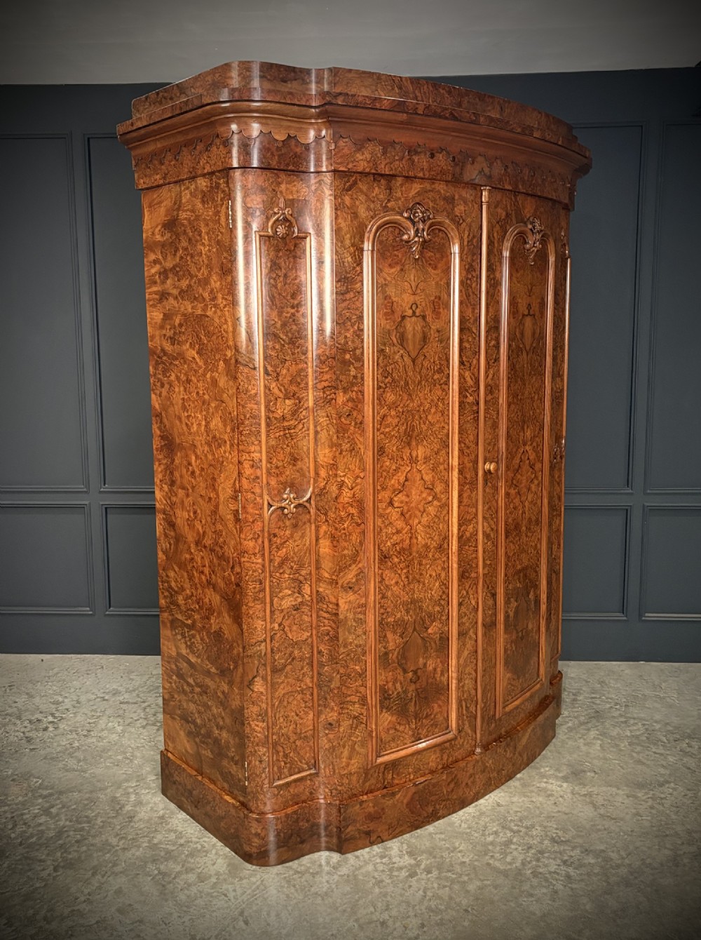 A large Victorian burr walnut bow-front wardrobe featuring carved arched door panels, a moulded cornice, and a plinth base.