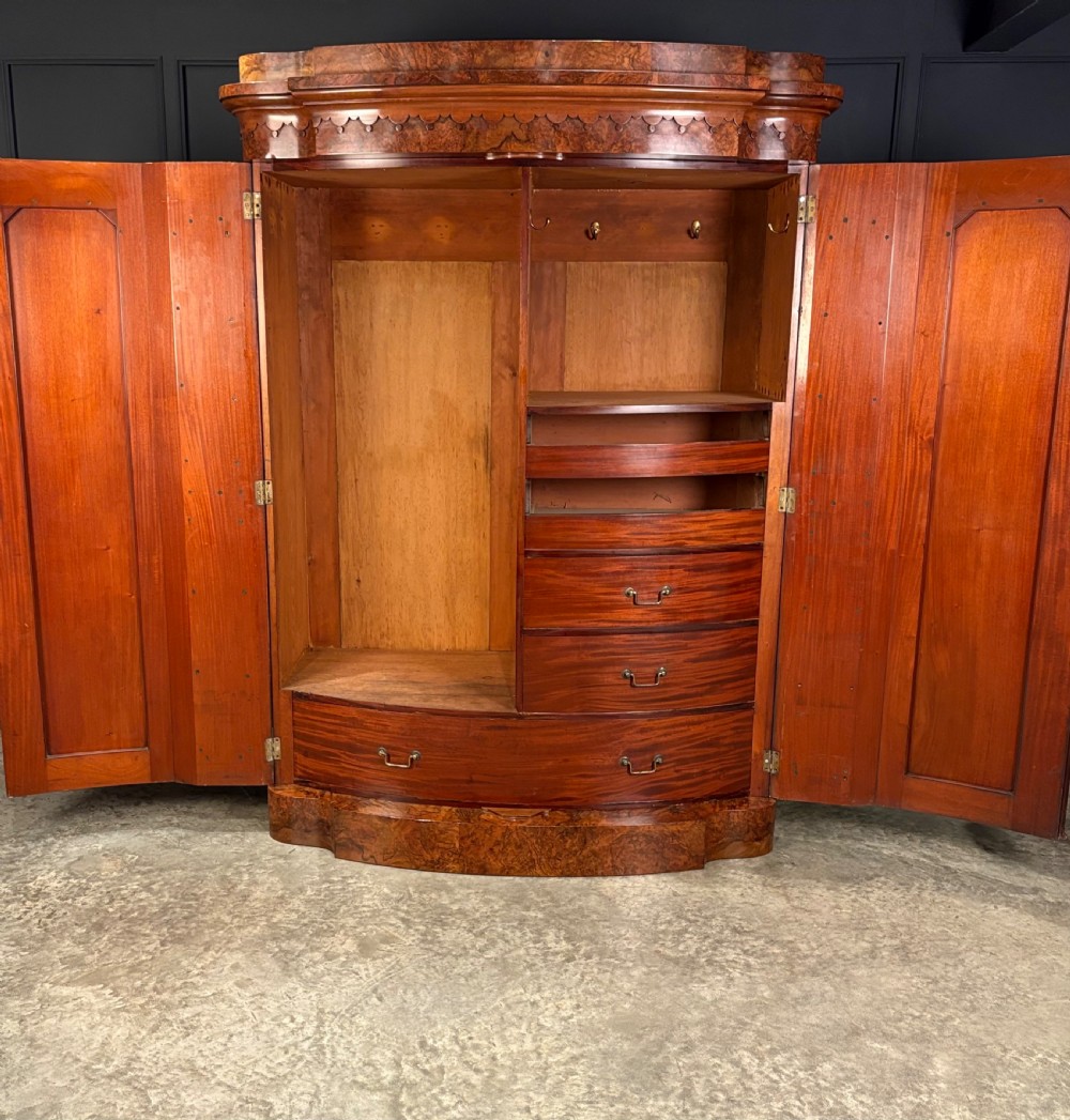 A large Victorian burr walnut bow-front wardrobe featuring carved arched door panels, a moulded cornice, and a plinth base. View V