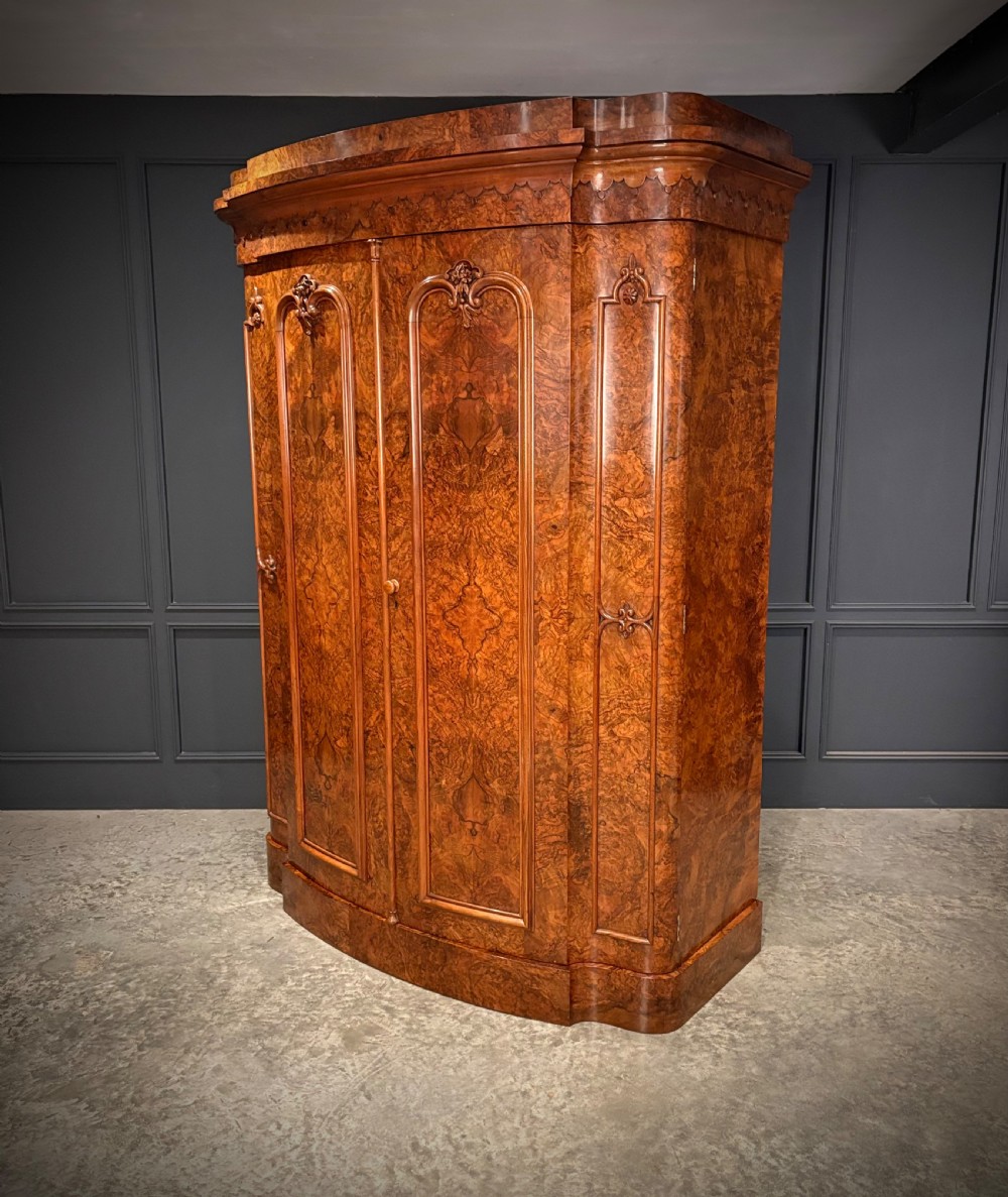 A large Victorian burr walnut bow-front wardrobe featuring carved arched door panels, a moulded cornice, and a plinth base. View VI