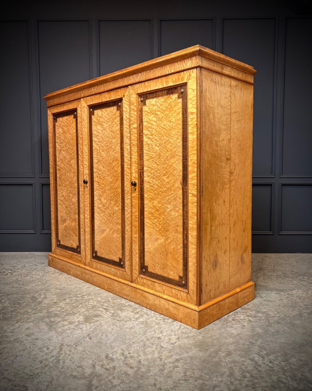 A low Victorian three-door wardrobe crafted from birds eye maple featuring dark wood inlaid borders and turned wooden knobs. View II