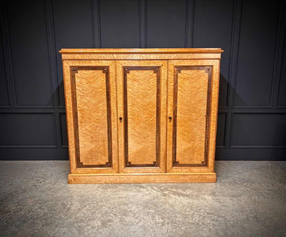 A low Victorian three-door wardrobe crafted from birds eye maple featuring dark wood inlaid borders and turned wooden knobs. View VI