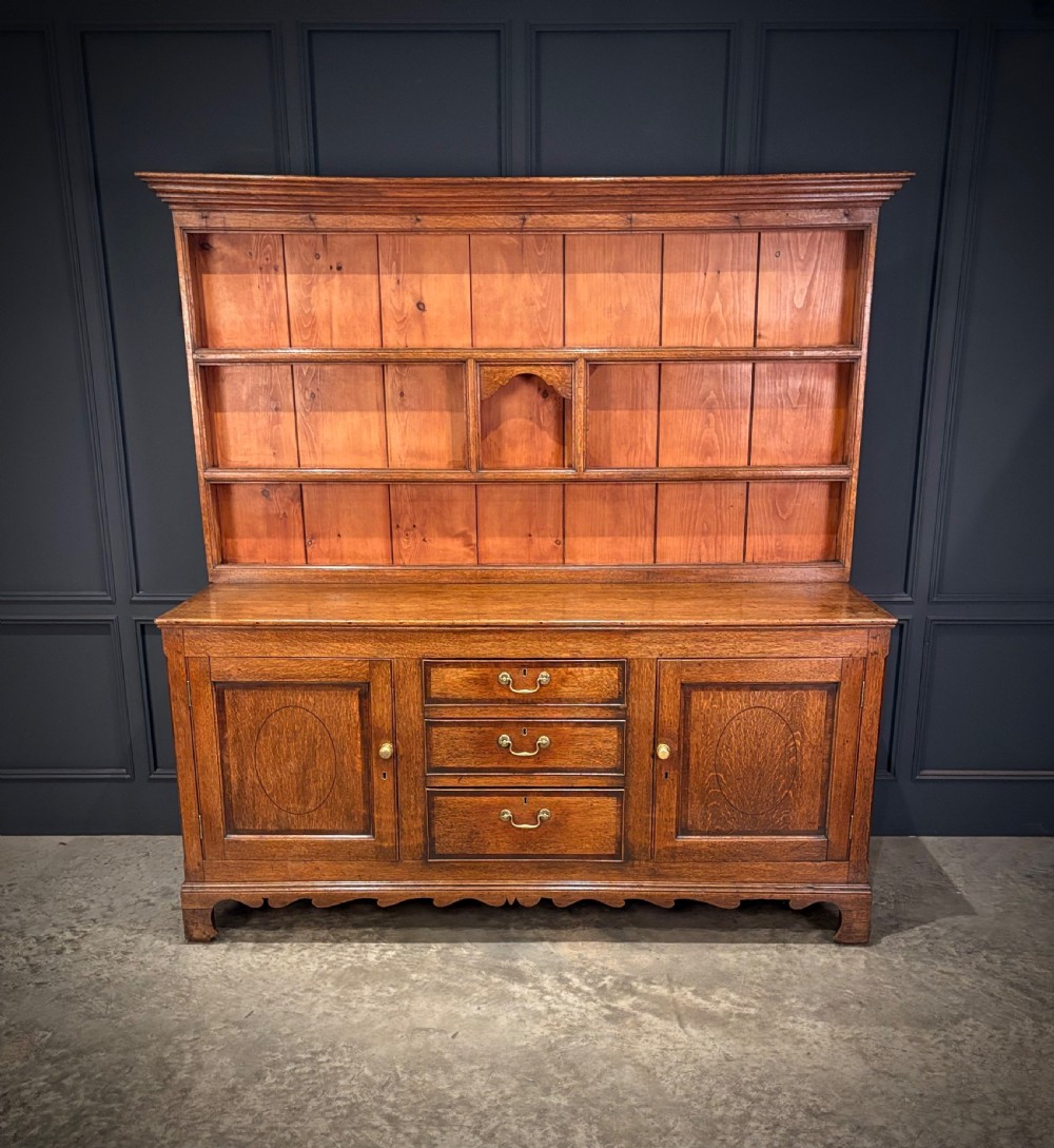 An eighteenth-century oak welsh dresser featuring a three-shelf open upper rack and a lower base with three drawers and two panelled cupboard doors.