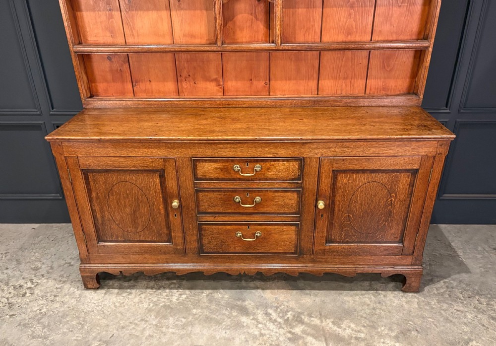 An eighteenth-century oak welsh dresser featuring a three-shelf open upper rack and a lower base with three drawers and two panelled cupboard doors. View V