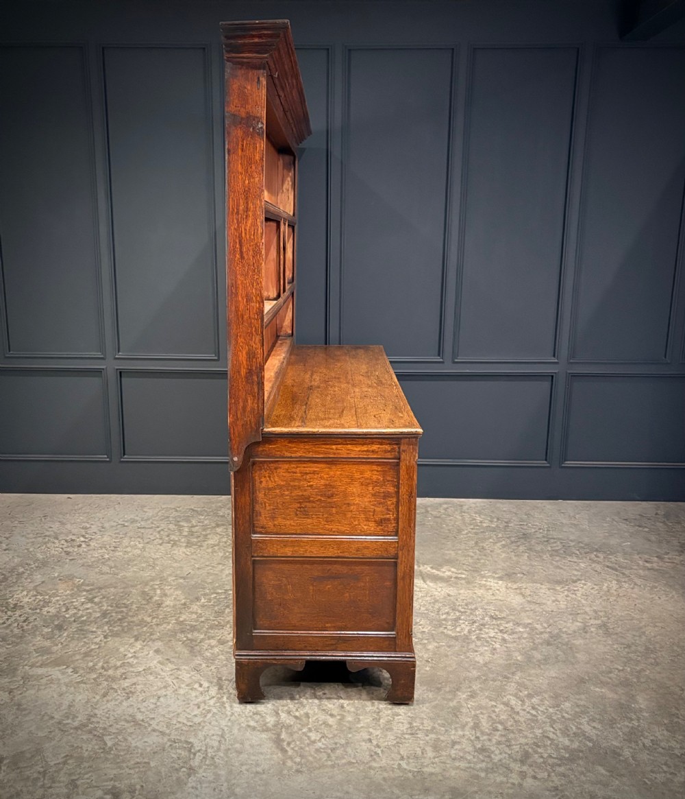An eighteenth-century oak welsh dresser featuring a three-shelf open upper rack and a lower base with three drawers and two panelled cupboard doors. View XV
