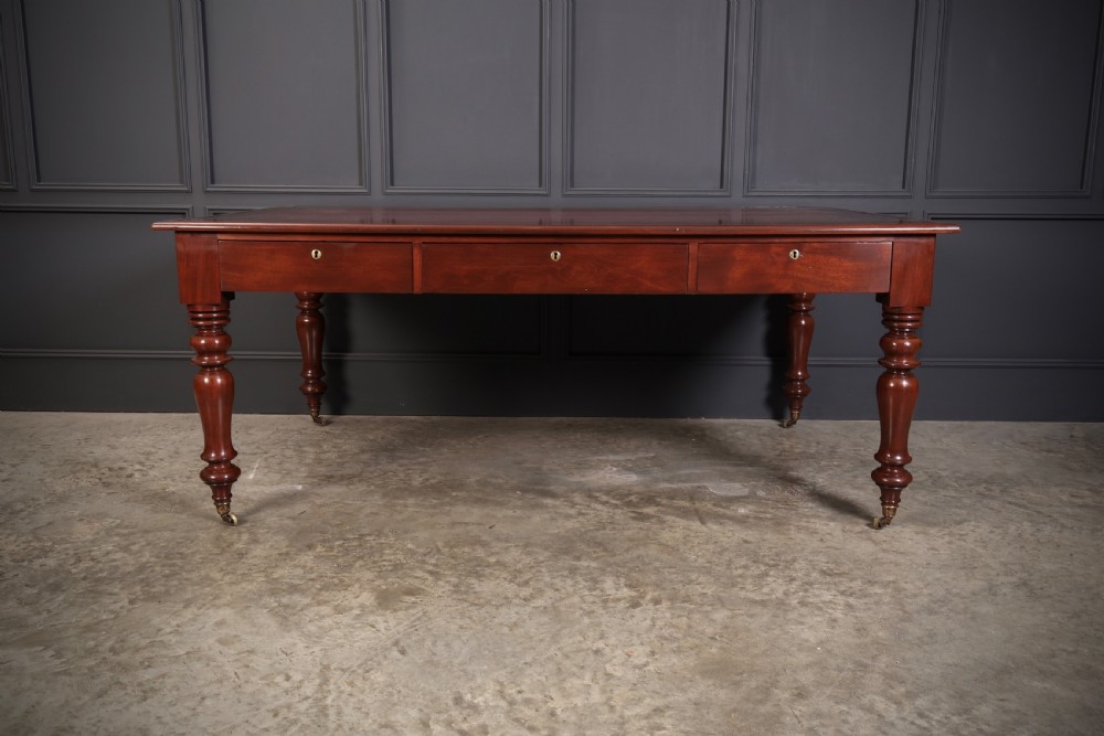 A Victorian mahogany partners writing table with a rich red leather inlaid top, frieze drawers, and turned legs set on brass castors. View IV