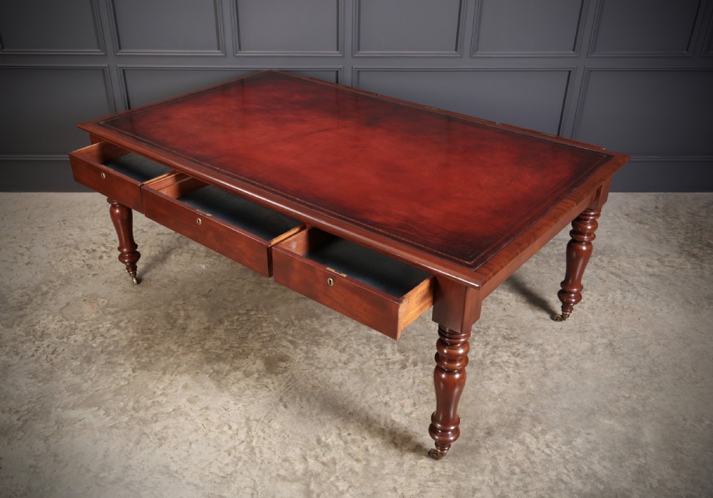 A Victorian mahogany partners writing table with a rich red leather inlaid top, frieze drawers, and turned legs set on brass castors. View IX