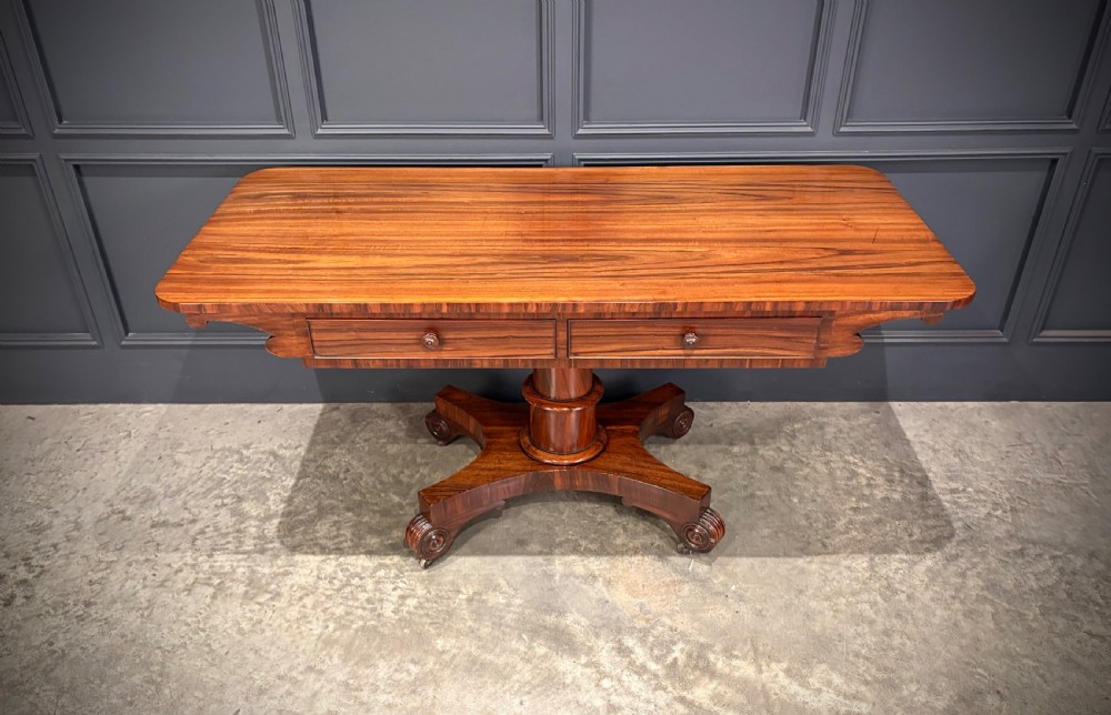 A 19th-century Goncalo Alves library table featuring a polished rectangular top with rounded corners, frieze drawers, and a central turned pedestal on a quadform base with scroll feet.