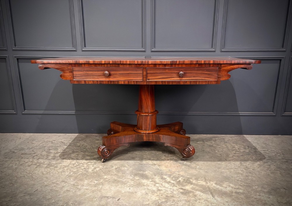 A 19th-century Goncalo Alves library table featuring a polished rectangular top with rounded corners, frieze drawers, and a central turned pedestal on a quadform base with scroll feet. View IV