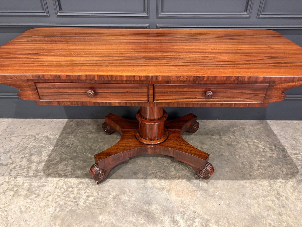 A 19th-century Goncalo Alves library table featuring a polished rectangular top with rounded corners, frieze drawers, and a central turned pedestal on a quadform base with scroll feet. View V
