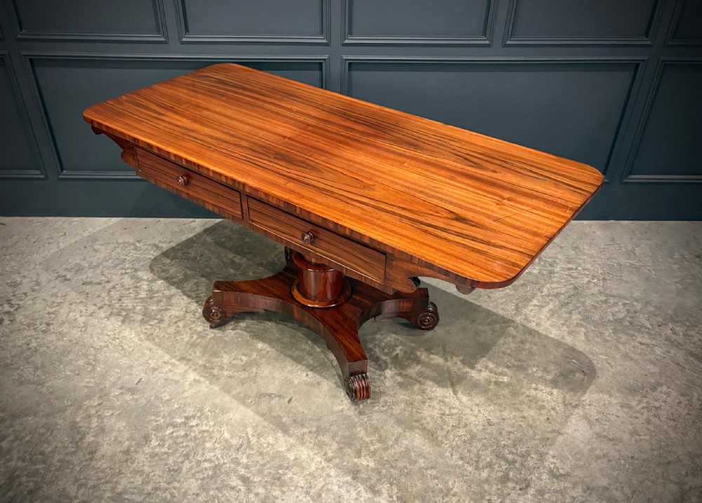 A 19th-century Goncalo Alves library table featuring a polished rectangular top with rounded corners, frieze drawers, and a central turned pedestal on a quadform base with scroll feet. View VI
