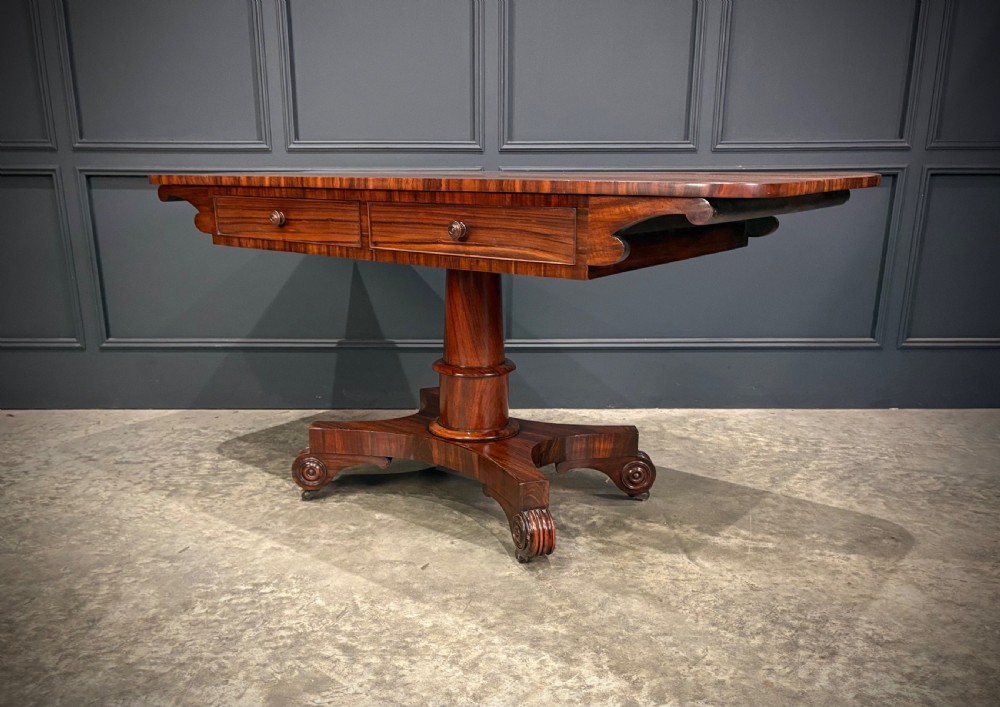 A 19th-century Goncalo Alves library table featuring a polished rectangular top with rounded corners, frieze drawers, and a central turned pedestal on a quadform base with scroll feet. View VII