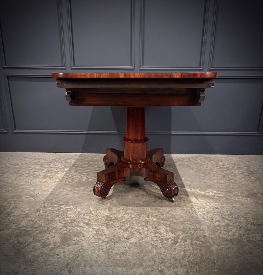 A 19th-century Goncalo Alves library table featuring a polished rectangular top with rounded corners, frieze drawers, and a central turned pedestal on a quadform base with scroll feet. View X