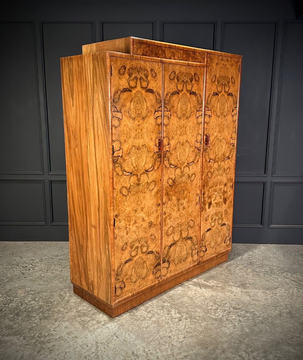 A tall three-door Art Deco wardrobe crafted from figured burr walnut with a stepped top cornice and plinth base.