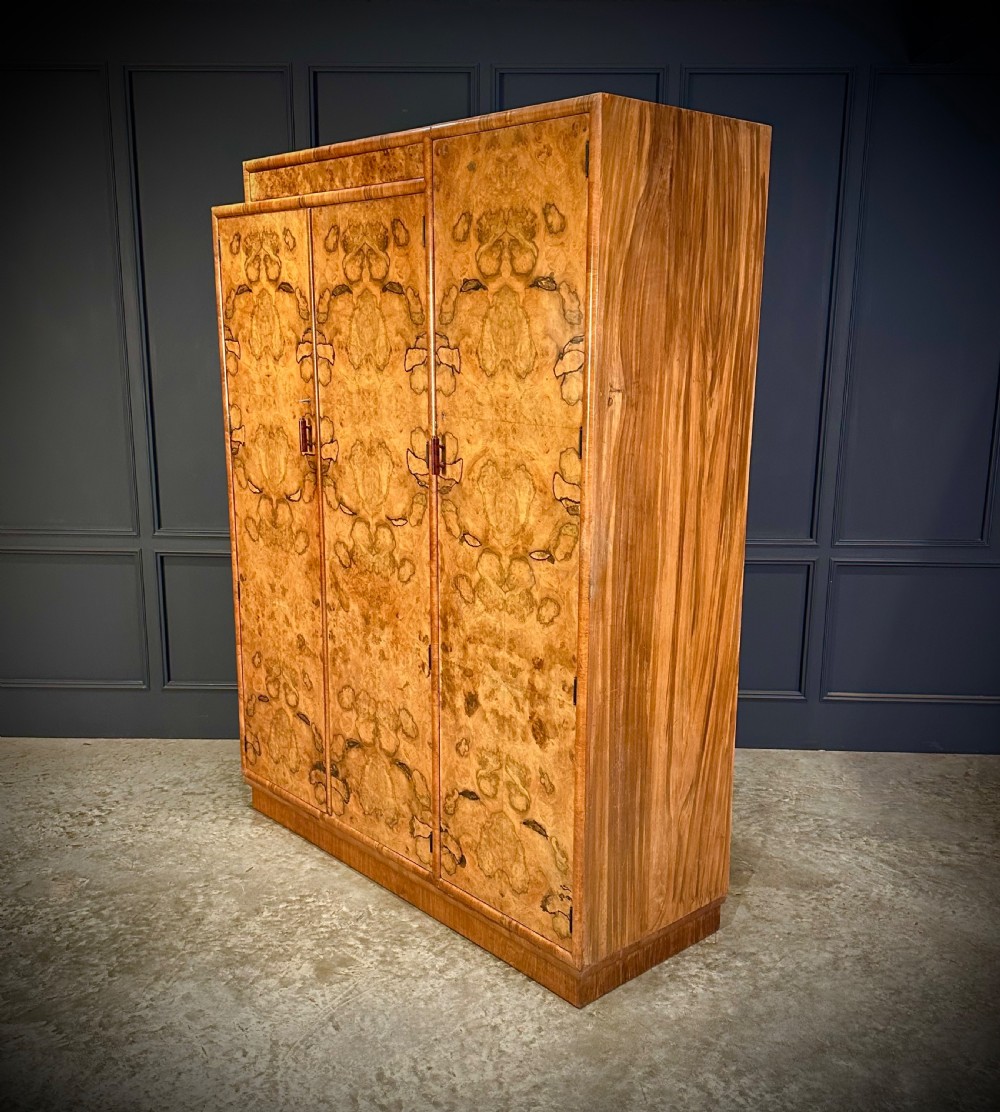 A tall three-door Art Deco wardrobe crafted from figured burr walnut with a stepped top cornice and plinth base. View IV