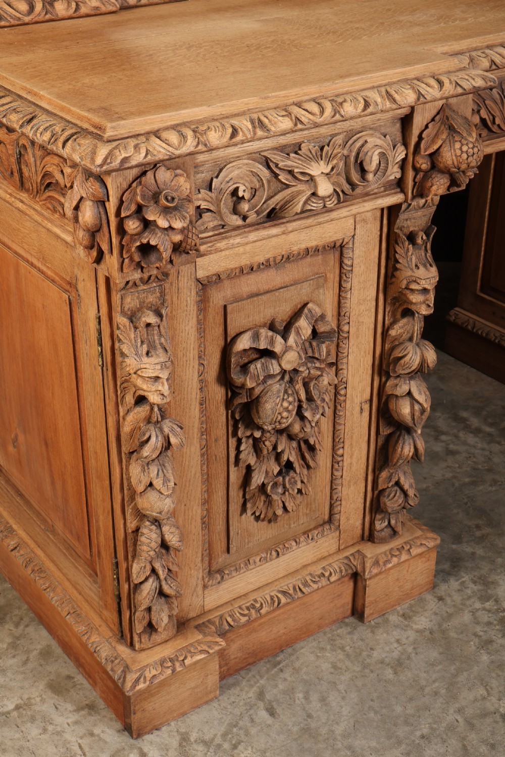 A large bleached oak pedestal sideboard featuring elaborate fruit swags, carved mask details, twin lower cupboards, and an integrated rectangular mirror superstructure. View II